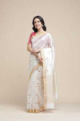 Woman wearing a white saree with a gold border on a beige background