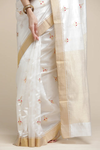 White saree with gold border and floral patterns on a beige background