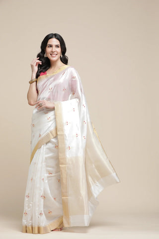 Woman wearing a white saree with gold border on a beige background