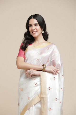 Woman wearing a white saree with a pink blouse against a beige background