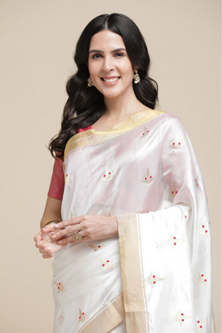 Woman wearing a white saree with gold border on a beige background