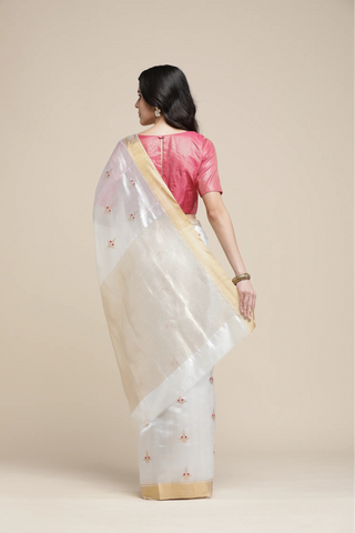 Woman wearing a white saree with gold border and pink blouse against a beige background