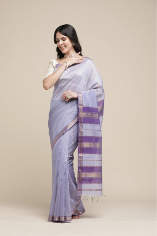 Woman wearing a light gray saree with purple stripes on a beige background