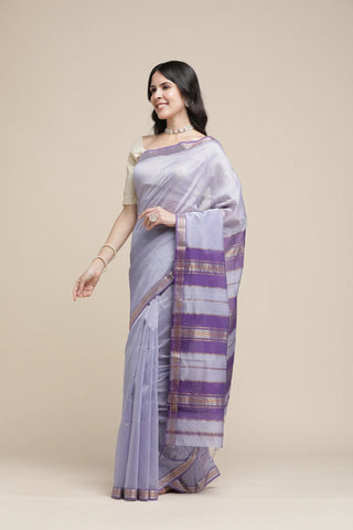 Woman wearing a light purple saree with a striped border on a beige background