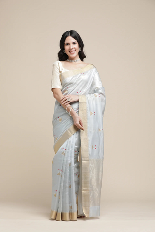 Woman wearing a light-colored saree with a beige border on a plain background