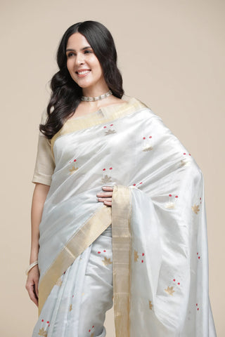 Woman wearing a white saree with gold border on a beige background