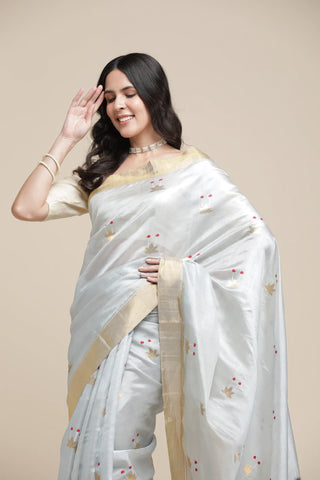 Woman wearing a white saree with gold border on a beige background