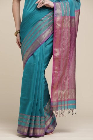 Teal saree with pink and gold border on a beige background