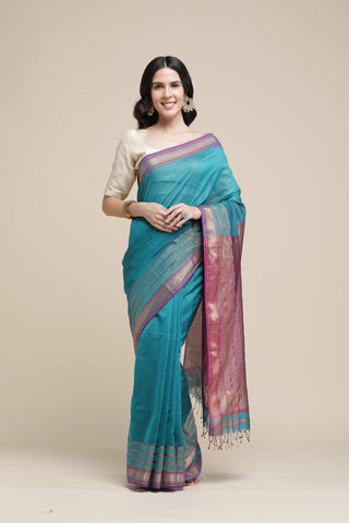 Woman wearing a teal saree with a white blouse against a beige background