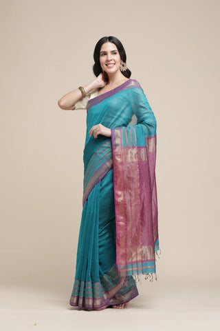 Woman wearing a teal saree with pink border on a beige background