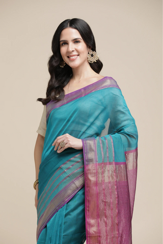 Woman wearing a teal and purple saree with a beige background
