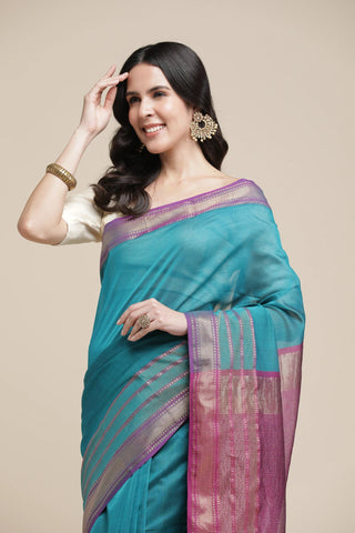 Woman wearing a teal saree with pink border on a beige background