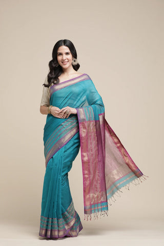 Woman wearing a turquoise saree with a pink border on a beige background