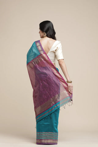 Woman wearing a purple and teal saree with a beige background