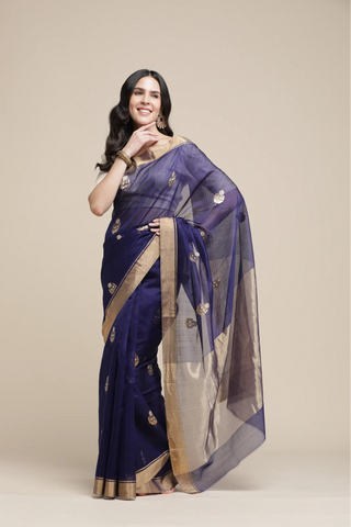 Woman wearing a purple saree with gold border on a beige background