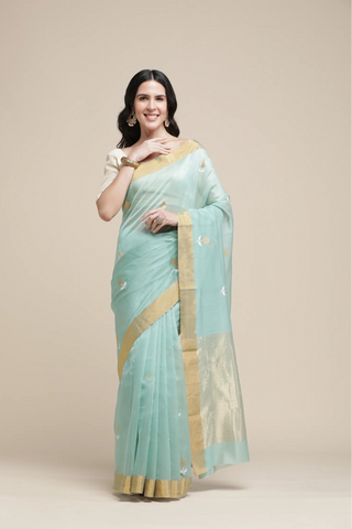 Woman wearing a light blue saree with gold border on a beige background