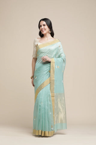 Woman wearing a light blue saree with a gold border on a beige background