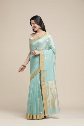Woman wearing a light blue saree with gold border on a beige background