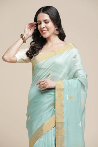 Woman wearing a light blue saree with gold border on a beige background