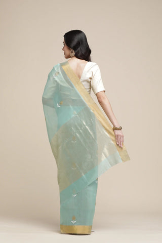 Woman wearing a light blue saree with a gold border on a beige background