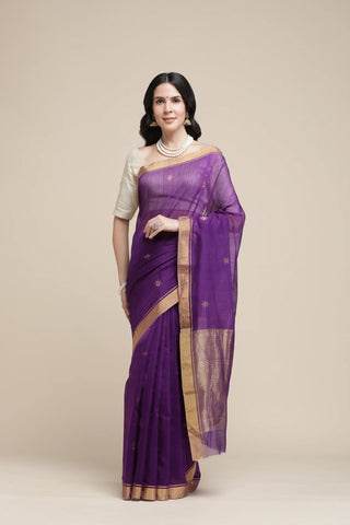 Woman wearing a purple saree with a beige blouse against a plain background