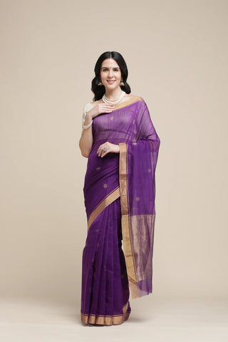 Woman wearing a purple saree with a gold border on a beige background