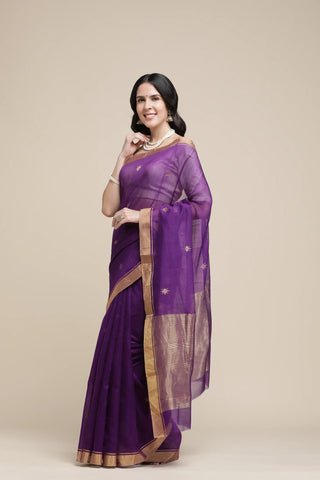 Woman wearing a purple saree with a gold border on a beige background