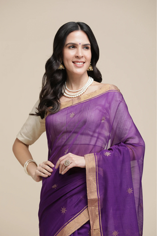 Woman wearing a purple saree with a beige blouse on a beige background