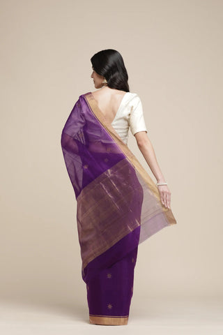 Woman wearing a purple saree with a beige border on a plain background