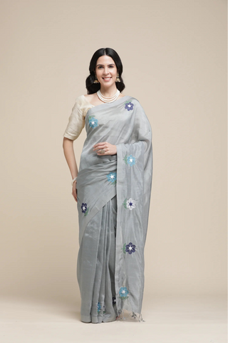 Woman wearing a light gray saree with floral patterns on a beige background