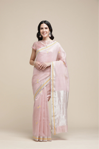 Woman wearing a light pink saree with a white blouse against a beige background