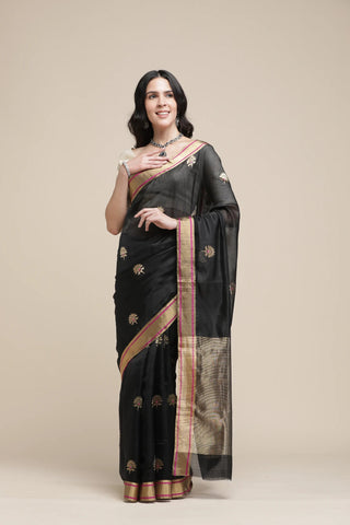 Woman wearing a black saree with gold border on a beige background
