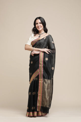 Woman wearing a black saree with gold border on a beige background