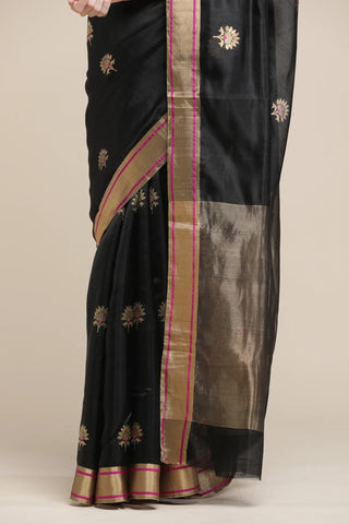 Black saree with gold and pink border on a beige background