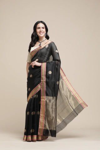 Woman wearing a black saree with gold border on a beige background