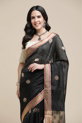 Woman wearing a black saree with gold and pink border on a beige background