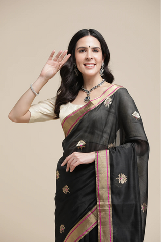 Woman wearing a black saree with gold patterns on a beige background