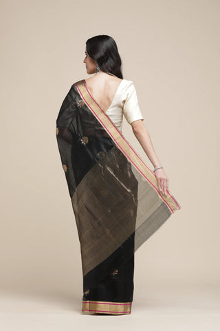 Woman wearing a black saree with a white blouse against a beige background