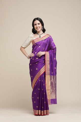Woman wearing a purple saree with gold border on a beige background