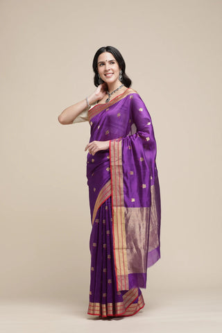 Woman wearing a purple saree with gold border on a beige background