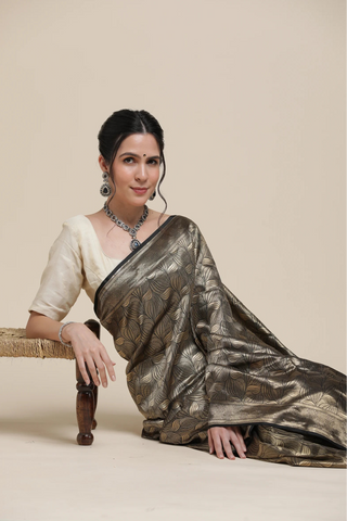 Woman wearing a saree sitting on a chair against a plain background