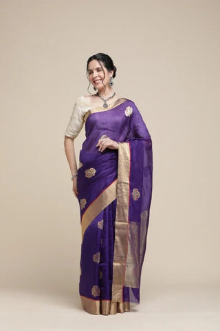 Woman wearing a purple saree with gold patterns on a beige background
