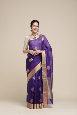 Woman wearing a purple saree with gold border on a beige background