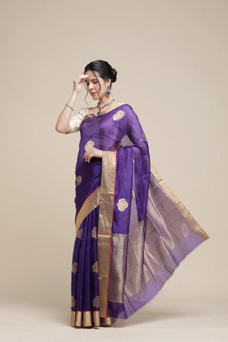 Woman wearing a purple saree with gold border on a beige background