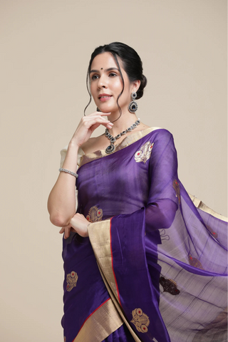 Woman wearing a purple saree with gold border against a beige background