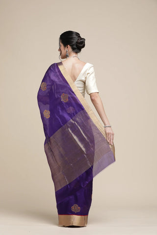 Woman wearing a purple saree with gold patterns on a beige background