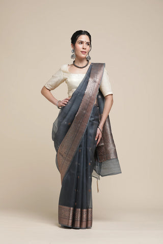 Woman wearing a dark gray saree with a brown border on a beige background