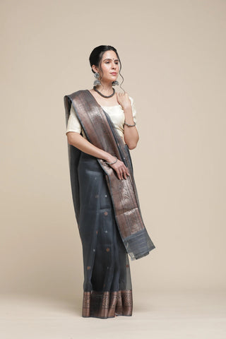 Woman wearing a black saree with a brown border on a beige background