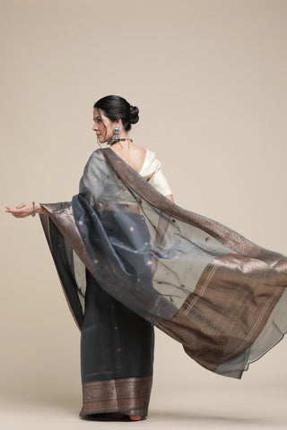 Woman wearing a black saree with a brown border on a beige background