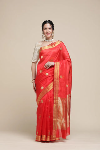Woman wearing a red saree with gold border on a beige background